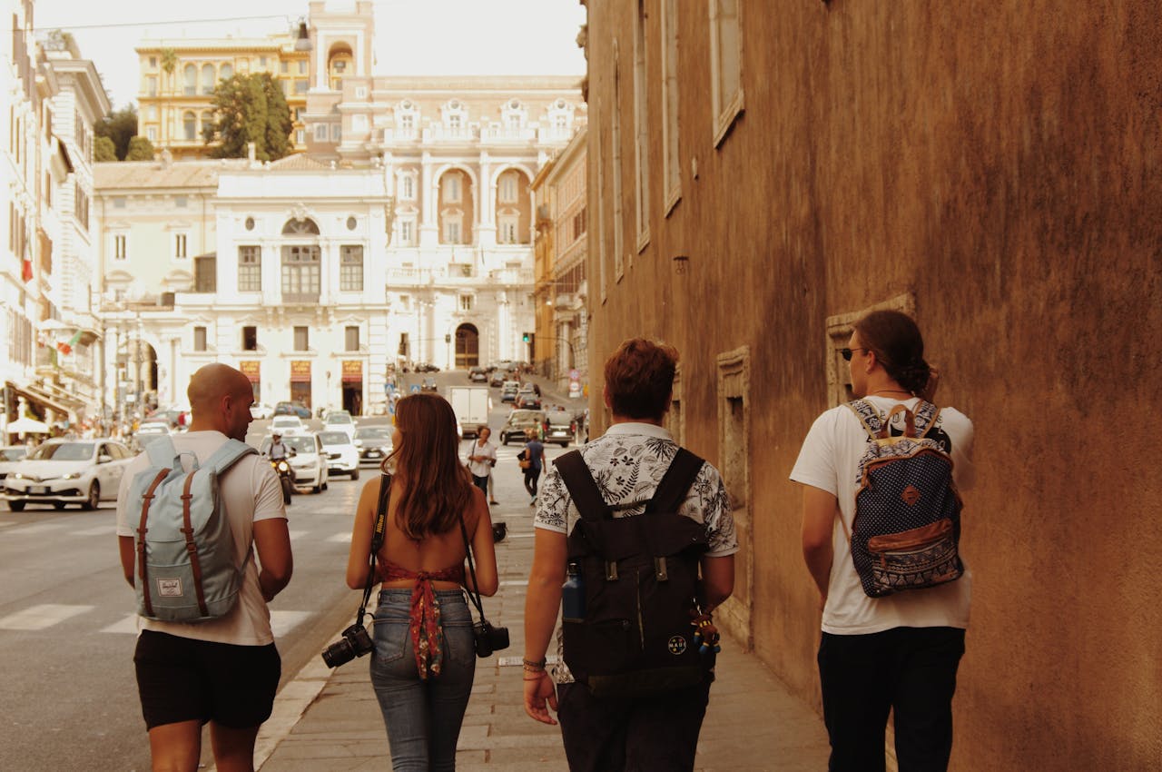 creative Four tourists with backpacks walking on a street in Rome, Italy, with historic architecture around.