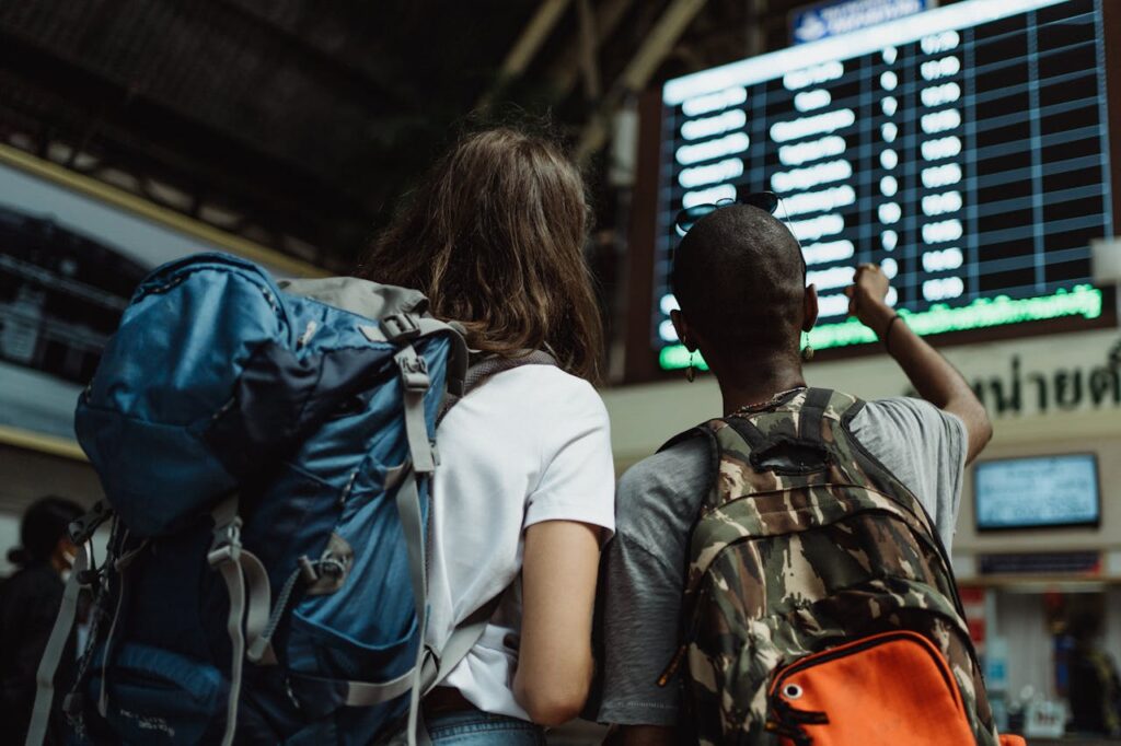 The Art of Drawing Readers In: Your attractive post title goes here Two backpackers checking the digital board at a train station for travel information.