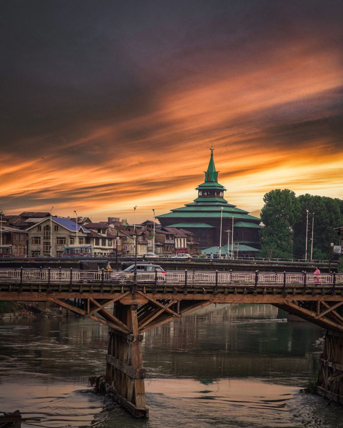 Beautiful sunset over a historic bridge and mosque in Srinagar, showcasing urban architecture and stunning skies.
